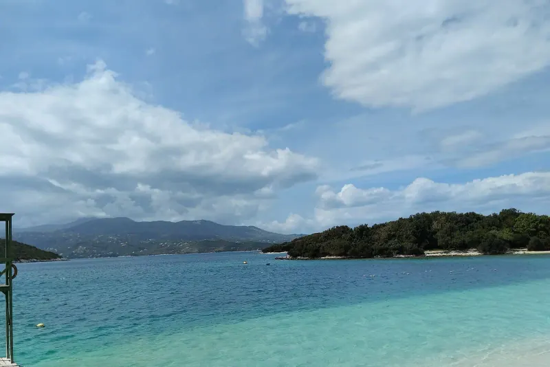 Turquoise shallow water and a pale sand beach at Ksamil with a wooded islet offshore and mountains behind