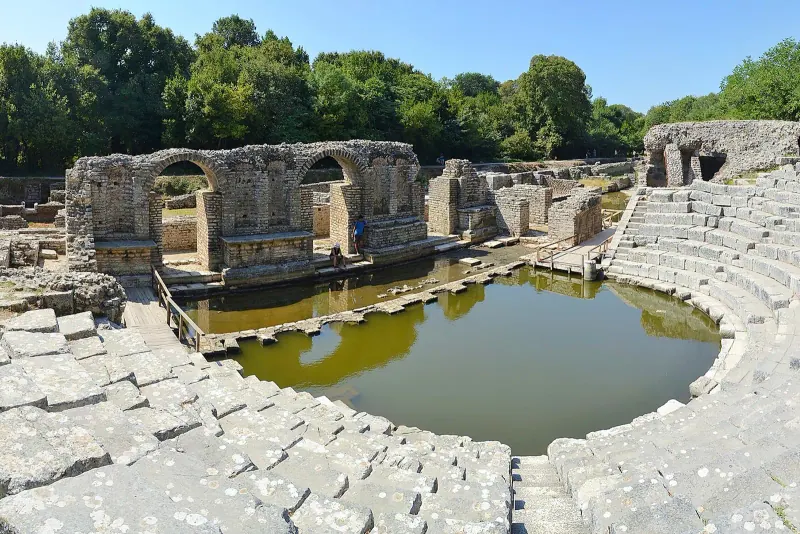 Stone seating tiers of the ancient theatre at Butrint with a pool of water in the orchestra