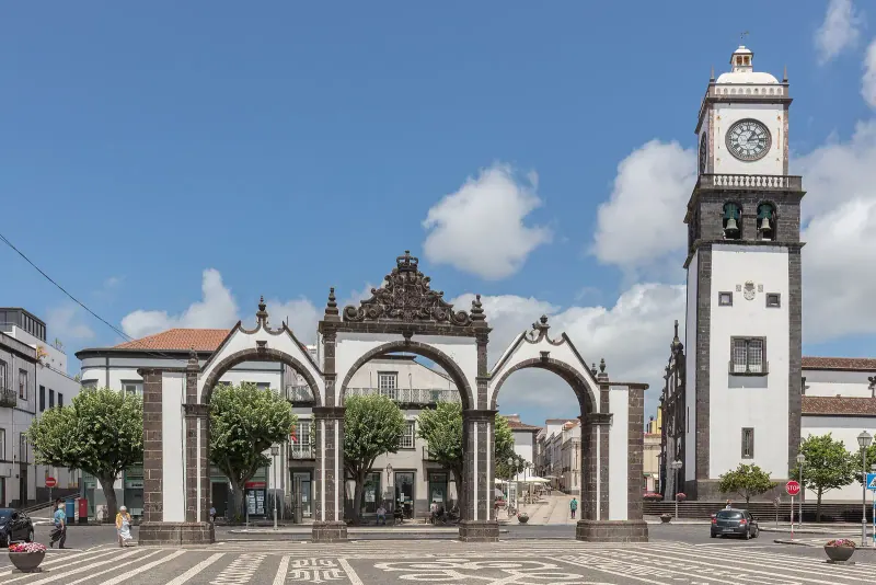 The three arched Portas da Cidade and clock tower on a paved square in Ponta Delgada under a blue sky
