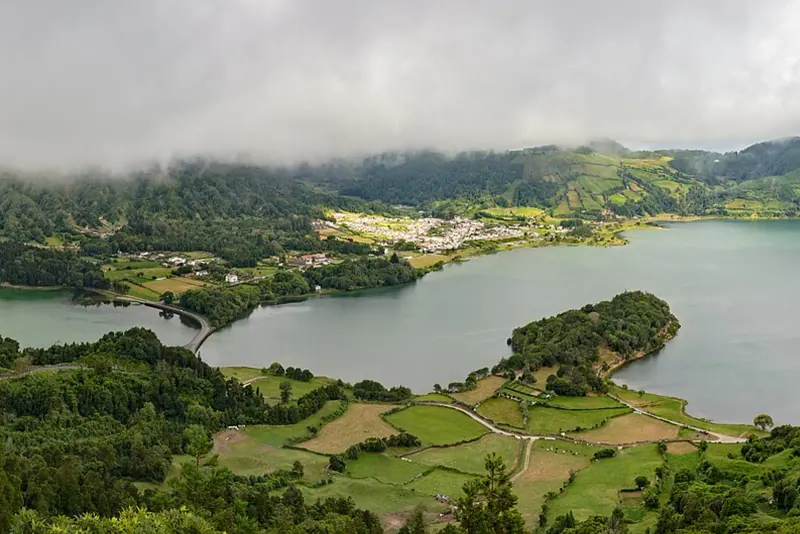 Green and blue crater lakes of Sete Cidades seen from a viewpoint, with farmland and low cloud over the rim