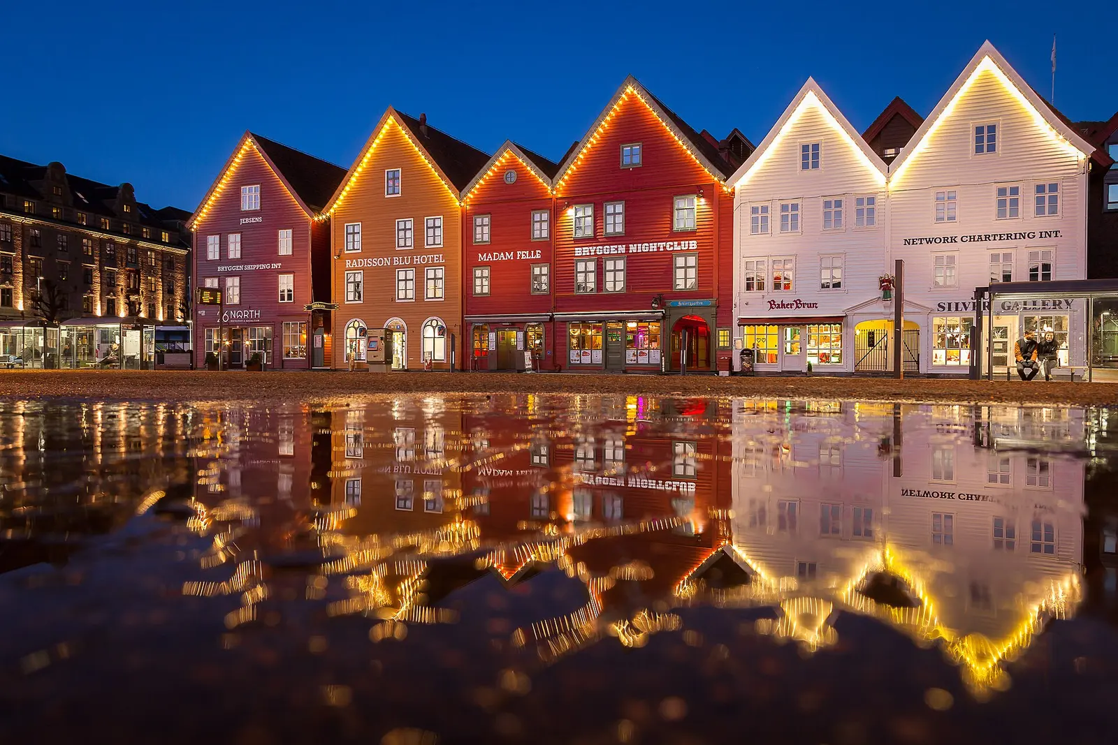 The wooden facades of Bryggen reflected in the harbour at night