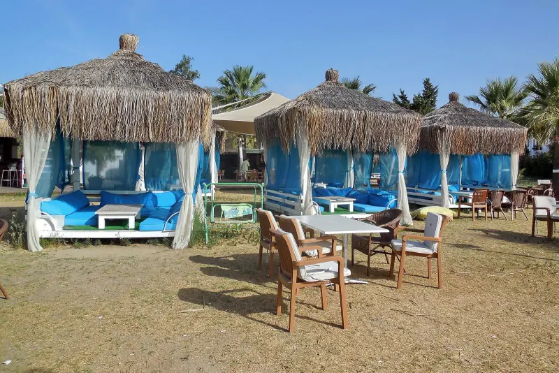 Thatched beach cabanas with blue drapes and chairs on the sand at a Bodrum beach club