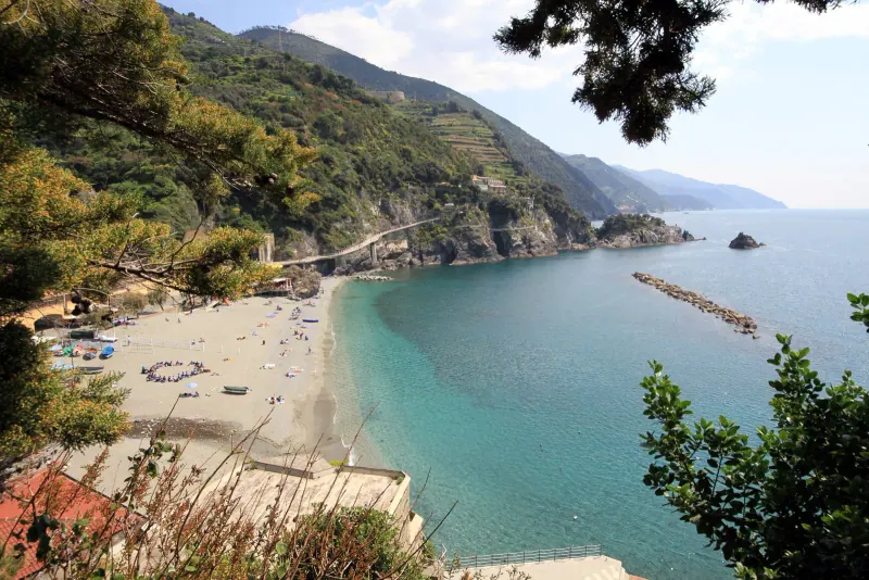 Sandy beach and turquoise water at Monterosso al Mare with a breakwater and wooded hills behind