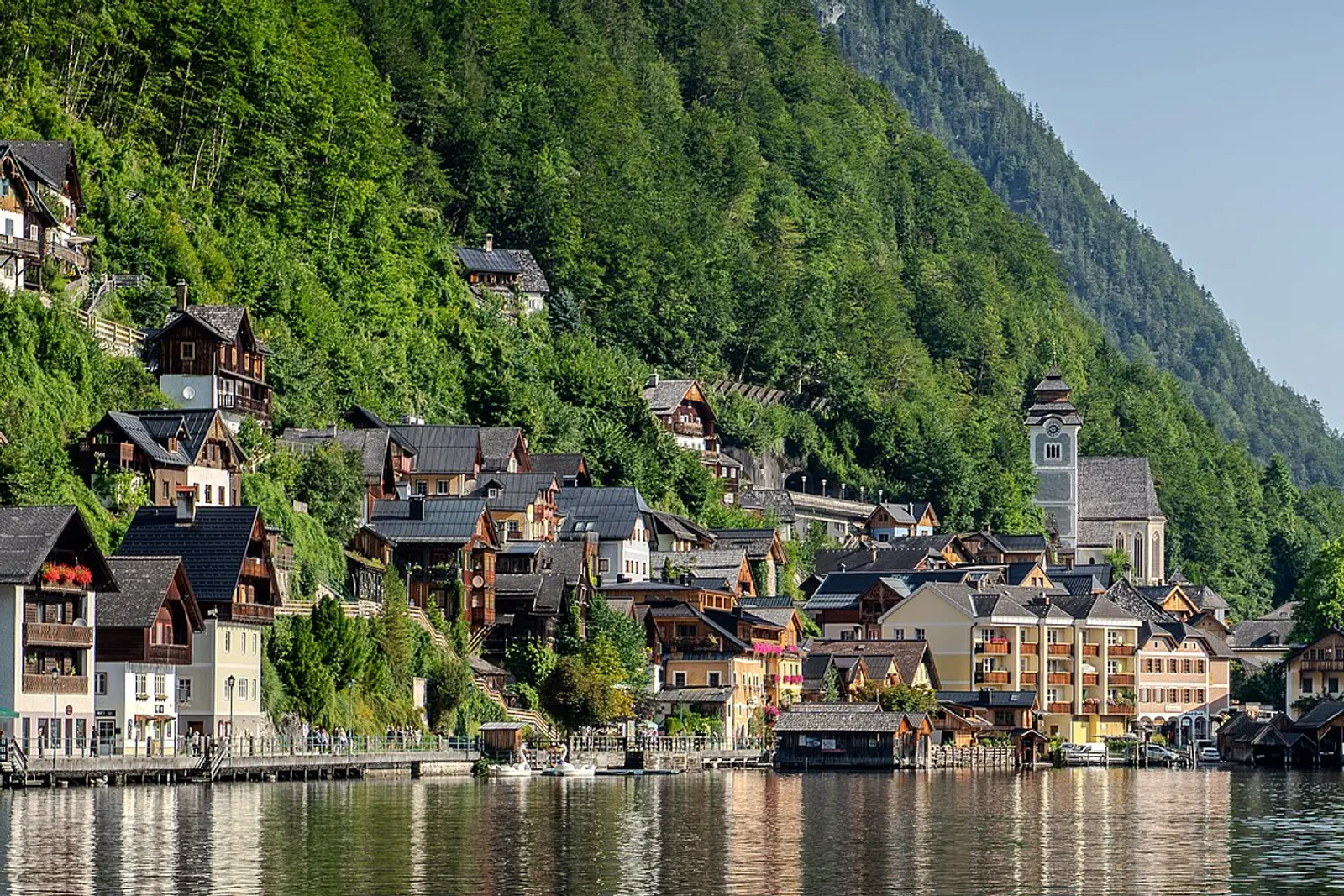 Hallstatt village houses and church on the lakeshore under steep wooded mountains