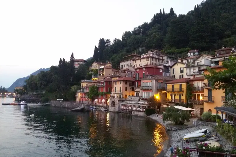 Colorful lakeside houses of Varenna glowing at dusk beside calm water with mountains behind