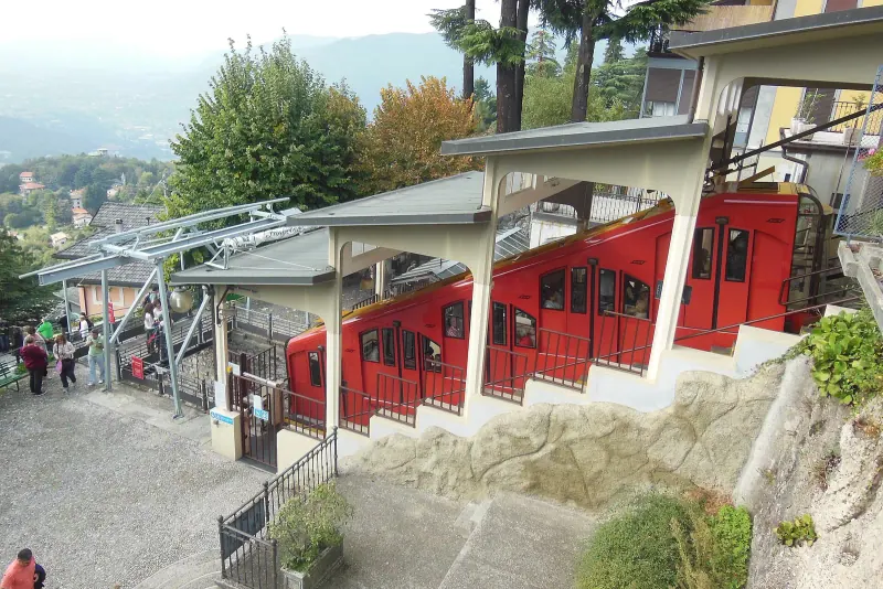 Red cars of the Como to Brunate funicular at the hillside station among trees and buildings
