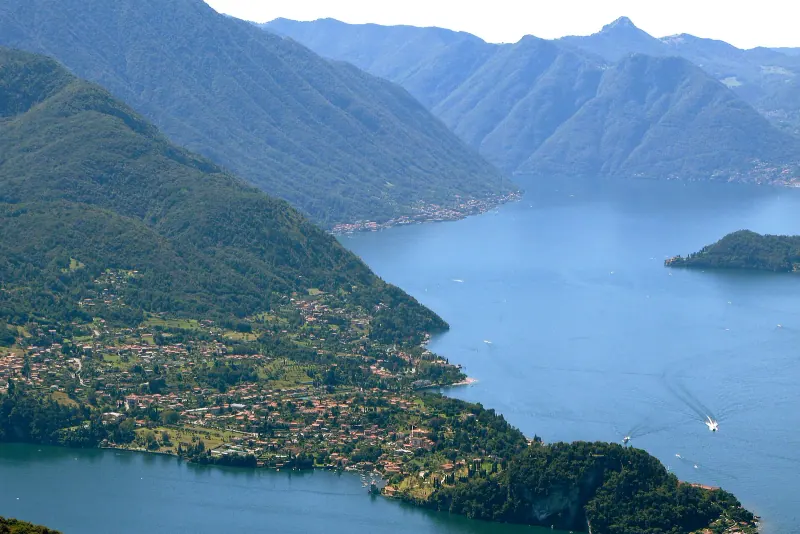 Aerial view of Lake Como's blue water and steep green mountainsides around a wooded promontory