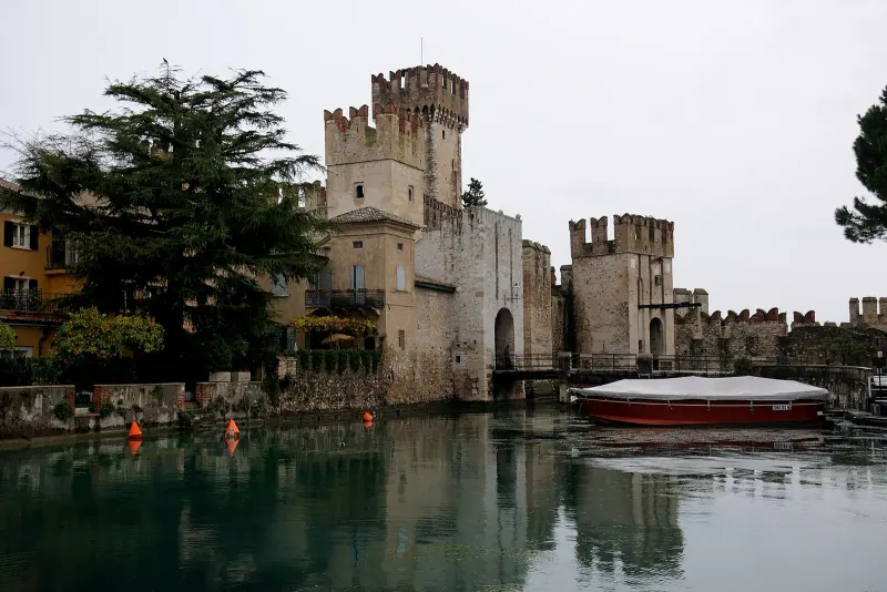 Scaligero Castle and its fortified harbour in Sirmione with calm water and a boat moored inside