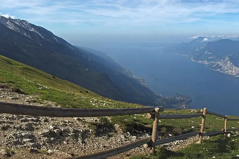 Lake Garda stretching between steep mountain slopes, seen from the grassy ridge of Monte Baldo