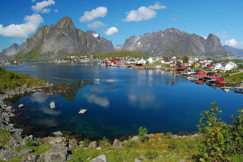 Red and white fishing cabins around a calm bay at Reine below jagged Lofoten peaks