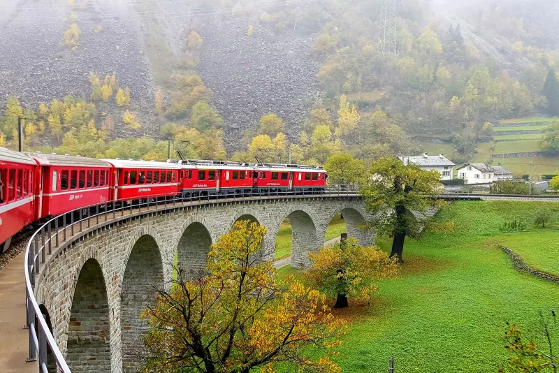 The red Bernina Express crossing a curved viaduct in the Alps