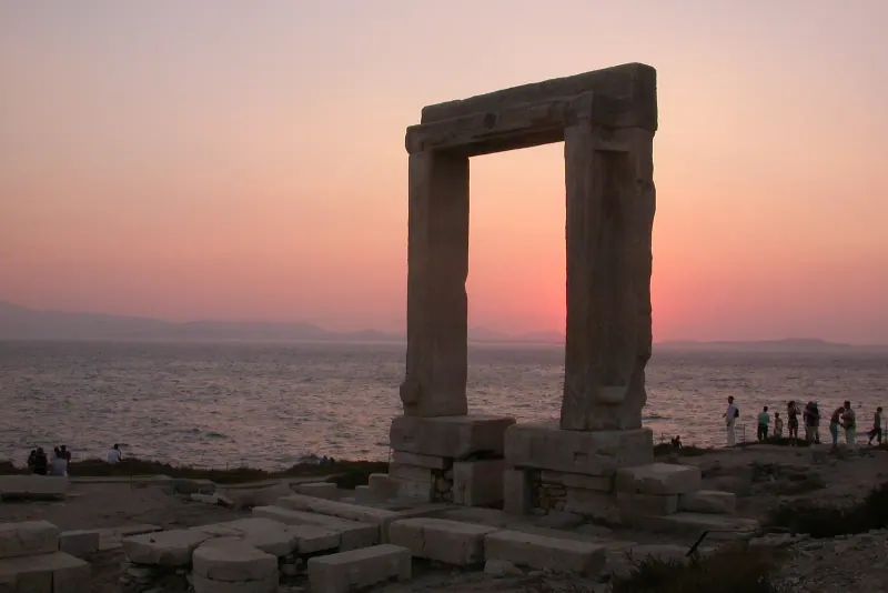 The marble Portara gateway on its rocky islet at sunset with an orange sky over the sea