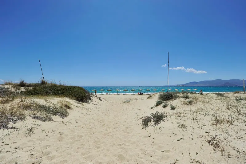 Sandy dune path leading down to a calm blue sea on Plaka beach under a clear sky