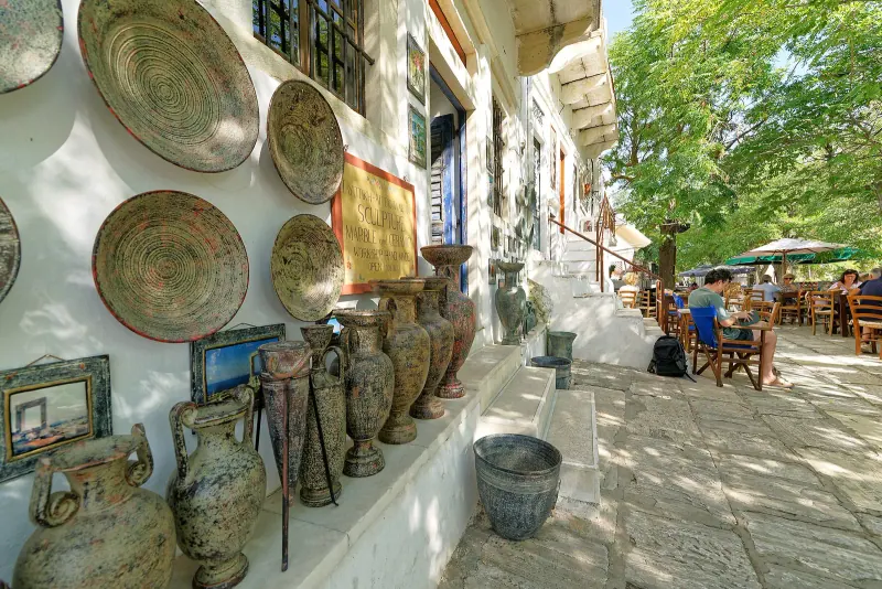 Shaded village lane in Apeiranthos lined with pottery displays and a cafe terrace
