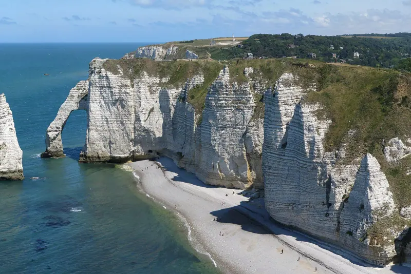 White chalk cliffs and the Aval arch and needle rock at Etretat above a pebble beach and blue sea