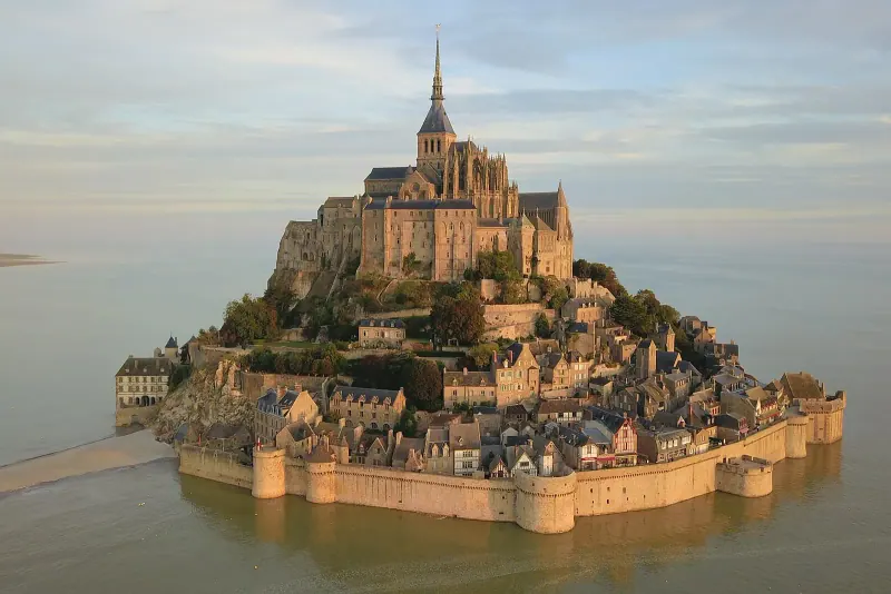 Aerial view of Mont-Saint-Michel abbey rising from the water at high tide in soft evening light