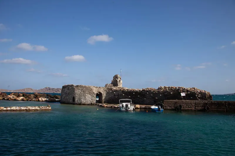 The ruined Venetian castle on a small rocky islet at the edge of Naoussa harbor under a blue sky