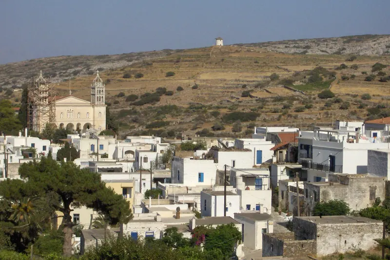 Whitewashed houses of Lefkes village climbing a dry hillside with a large church at the center