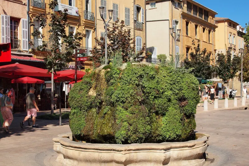 Moss-covered Fontaine Moussue on a sunny Aix-en-Provence square with cafe terraces and red awnings behind