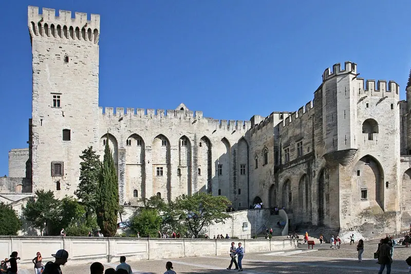 Pale stone towers and walls of the Palais des Papes rising above the square in Avignon