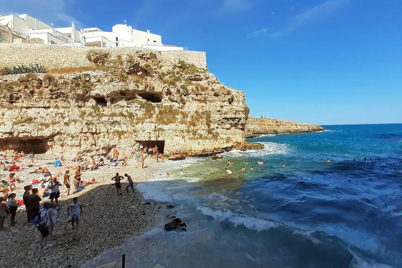Pebble cove below the white clifftop old town of Polignano a Mare with blue sea
