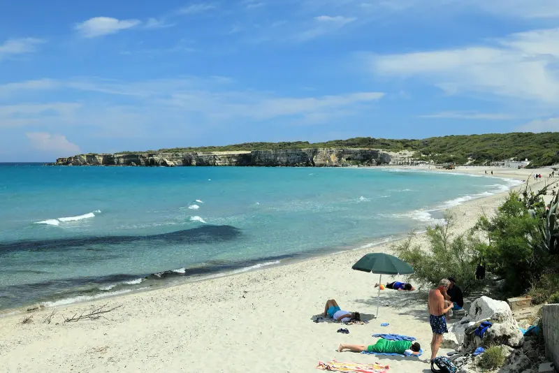 Sandy Salento beach curving along clear turquoise water with low cliffs in the distance