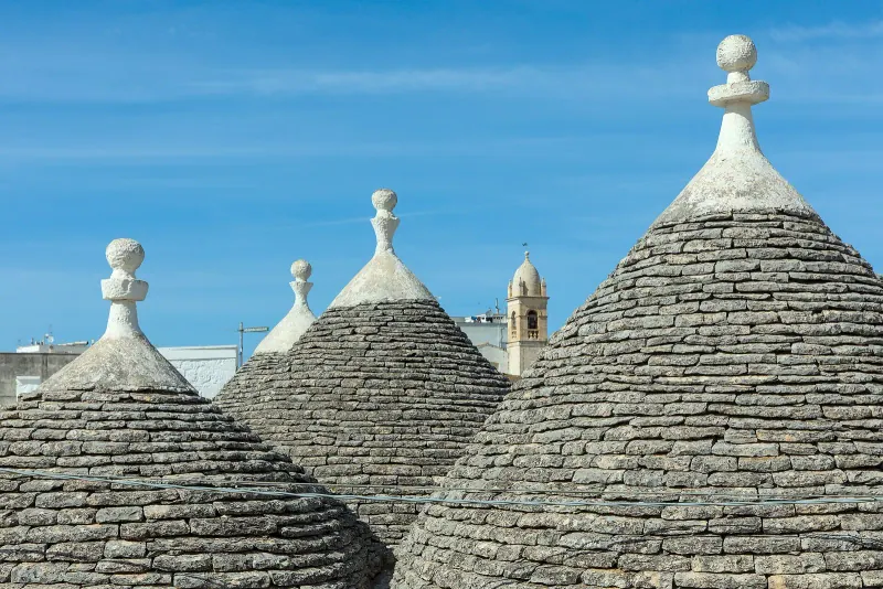 Grey conical stone roofs of trulli with white pinnacles in Alberobello under a blue sky