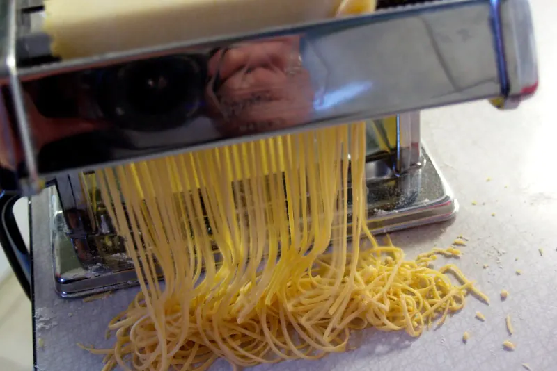 Fresh pasta coming out of a hand-cranked pasta machine