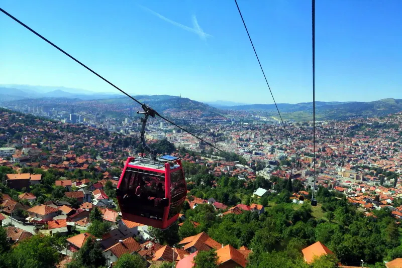 A red Trebevic cable car gondola crossing above Sarajevo with the city spread out below