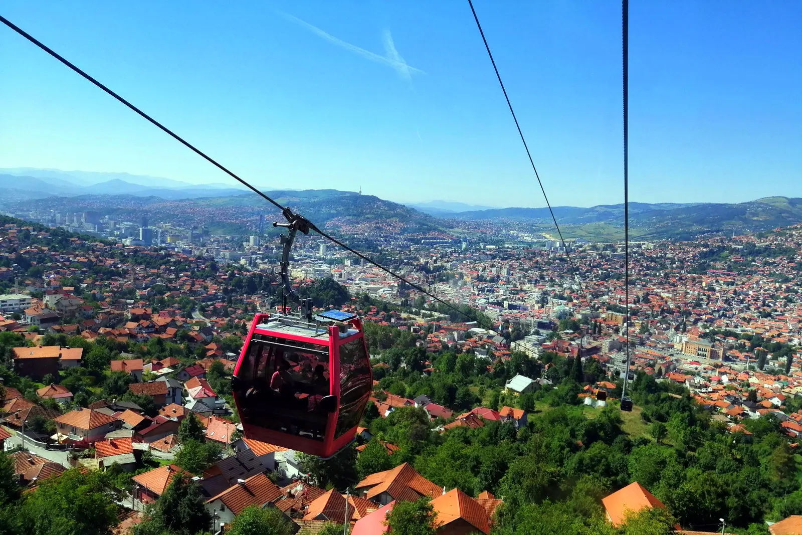 A red Trebevic cable car gondola crossing above Sarajevo with the city spread out below