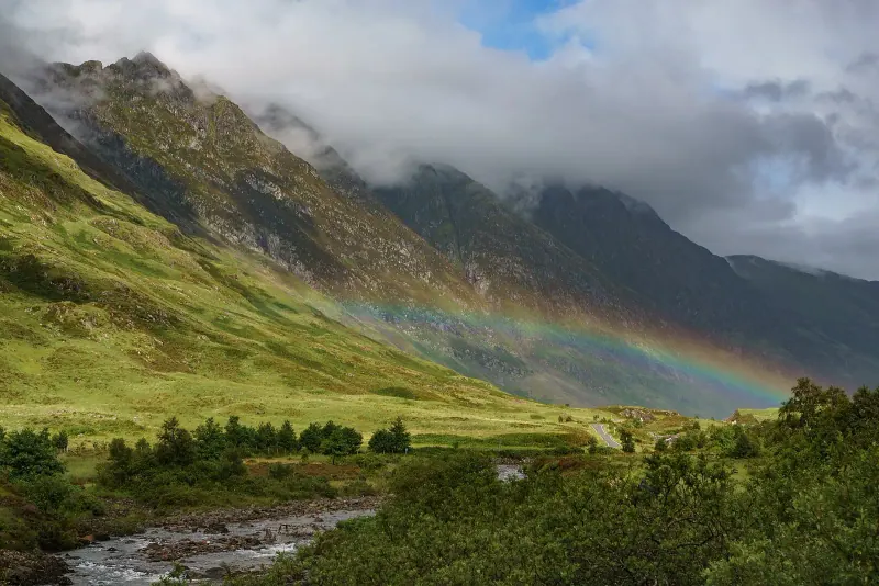 A rainbow over green slopes and a river in Glen Coe in the Scottish Highlands