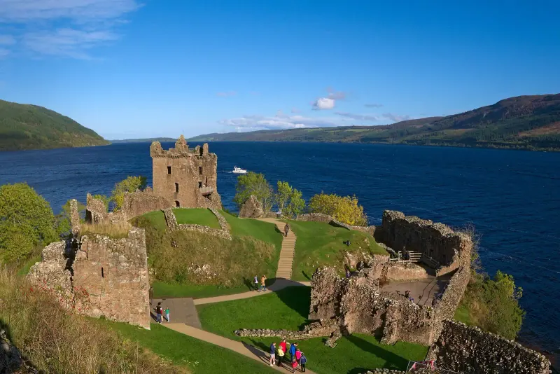 Ruins of Urquhart Castle on a grassy headland above the dark blue water of Loch Ness