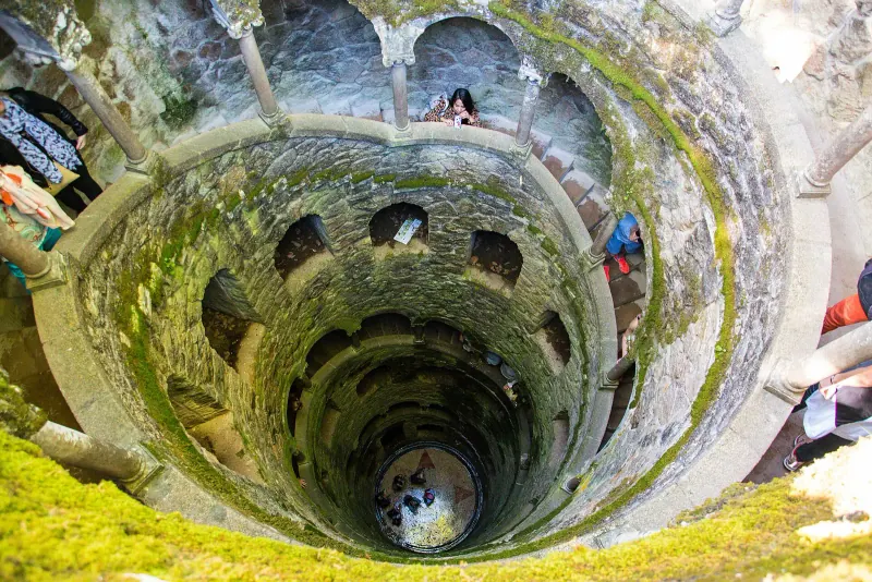 Spiral stone stairway of the Initiation Well at Quinta da Regaleira seen from above, covered in moss