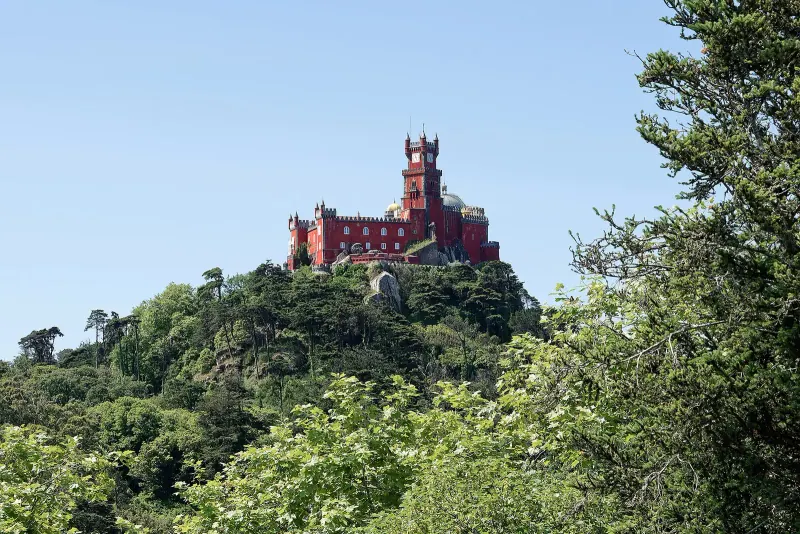 Red Pena Palace crowning a forested hilltop above the Sintra woods on a clear day